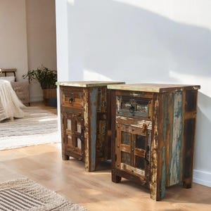 May include: Two wooden nightstands with a distressed finish. Each nightstand has a drawer and a door with a unique design. The nightstands are made of reclaimed wood and have a rustic look.