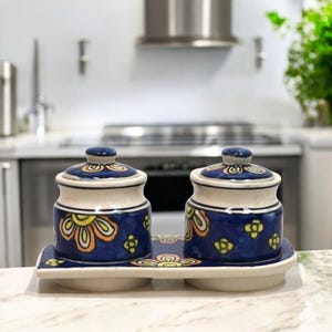 May include: Two blue and white ceramic jars with floral designs and lids, sitting on a matching tray.