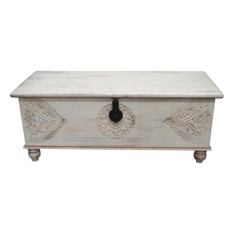 May include: White wooden storage chest with carved floral designs and a black metal latch. The chest has a distressed white finish and sits on four turned legs.