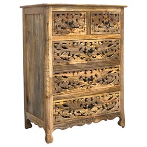 Op de afbeelding: Houten dressoir met vijf lades, twee kleine en drie grote. De lades zijn ingewikkeld gesneden met een bladeren ontwerp. Het dressoir is gemaakt van lichtbruin hout en heeft zwarte metalen handgrepen.