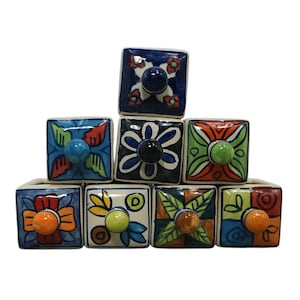 May include: A set of seven square ceramic drawer knobs arranged in a pyramid. Each knob features a unique hand-painted floral or geometric pattern in vibrant colors including blue, orange, green, and red, with a small round center handle.