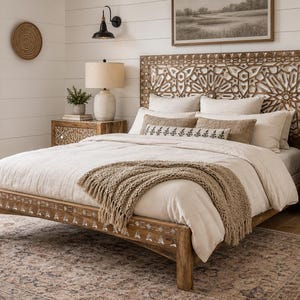 May include: A bedroom with a carved wooden bed frame and headboard. The bed is covered with white bedding and a tan fringed throw. Two matching nightstands with lamps flank the bed. A patterned rug and a window with a tree complete the scene.
