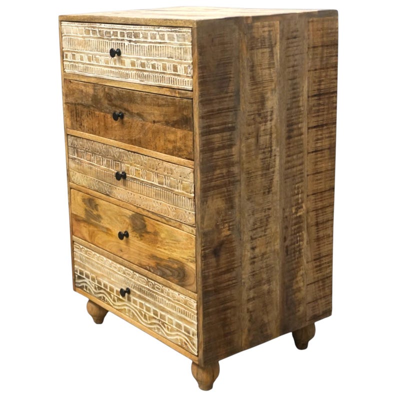 May include: A tall wooden chest of drawers with five drawers. The chest has a natural wood finish with carved details on some drawers and black knobs. It stands on four small, rounded feet. The wood grain is visible throughout.