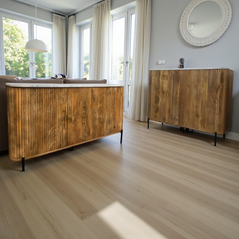 K&ouml;nnte beinhalten: Zwei Holzschr&auml;nke mit vertikalen Rillen und Marmorplatten. Die Schr&auml;nke sind warmbraun und stehen auf schwarzen Metallbeinen. Der Raum hat einen hellen Holzboden und gro&szlig;e Fenster mit wei&szlig;en Vorh&auml;ngen.