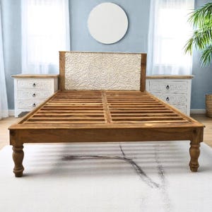 May include: A wooden bed frame with a carved headboard. The headboard is white and has a floral design. The bed frame is brown and has turned legs.