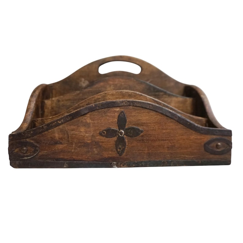 May include: A wooden desk organizer with three compartments and a handle. The organizer is brown with metal accents and a decorative four-petal design in the center. The edges are trimmed with metal.