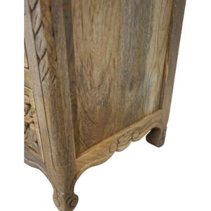 Op de afbeelding: Close-up van een houten kast met gesneden bloemendetails. De kast heeft een natuurlijke houten afwerking met zichtbare nerfpatronen. De poten zijn gebogen en voorzien van decoratieve gravures.