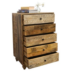 May include: A wooden chest of drawers with five drawers, each with a black knob. The drawers are open, revealing the interior. The top of the chest has books, a small box, and a vase with white flowers. The wood has a natural finish.