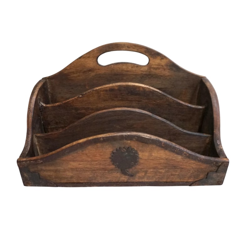 May include: A vintage wooden desk organizer with three tiered compartments and a handle. The organizer is stained a dark brown color and features a decorative emblem on the front. Metal corner accents add detail.