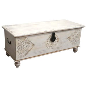May include: White wooden storage chest with carved details and a black metal latch. The chest has four legs and is a decorative piece of furniture.