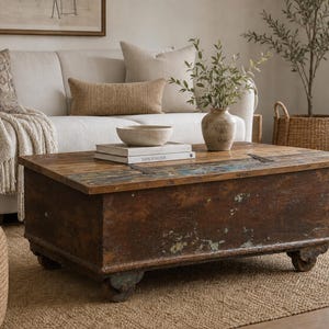 May include: A rectangular wooden coffee table featuring a weathered brown finish with visible traces of green paint. The table has a flat top surface, a sturdy box-like base, and is supported by four small wheels. It is positioned in a living space.