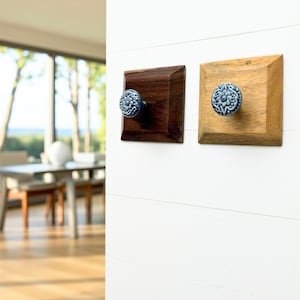 May include: Two square wooden wall hooks. One is dark brown, the other is light brown. Each has a blue and white floral ceramic knob. The hooks are mounted on a white wall, showcasing a decorative and functional design.