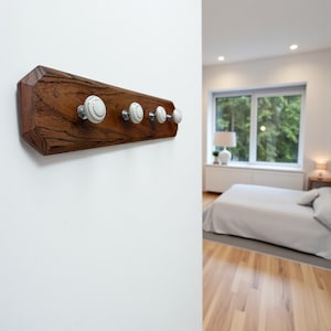 May include: A wooden coat rack with five white and silver knobs. The rack is made of dark brown wood and is mounted on a white wall. The knobs have a floral design.