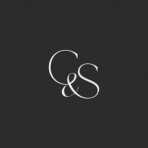 May include: A graphic logo design featuring the white serif letters C and S intertwined in a calligraphic script style. The letters are centred against a solid dark grey background, creating a high-contrast visual composition of the monogram.