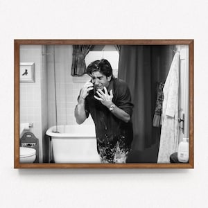 Puede incluir: Impresión enmarcada en blanco y negro de un hombre en un baño, hablando por teléfono y cubierto de jabón. El hombre está frente a una bañera blanca, con una toalla colgando de la pared.