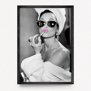 Könnte beinhalten: Schwarz-Weiß-Druck einer Frau, die sich rosa Lippenstift aufträgt. Sie trägt eine Sonnenbrille, ein Handtuch und einen Bademantel. Das Bild hat eine Vintage- und glamouröse Ästhetik, mit Fokus auf Schönheit und Stil.