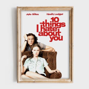 Op de afbeelding: Ingelijste filmposter voor "10 Things I Hate About You" met Julia Stiles en Heath Ledger. De titel staat in grote rode letters. De acteurs zitten in een bruine fauteuil. De lijst is lichtbruin van kleur.
