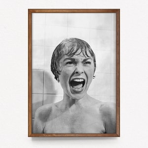 Könnte beinhalten: Gerahmter Schwarz-Weiß-Druck einer schreienden Frau in einer Dusche. Das Bild stammt aus einem klassischen Film, Wassertropfen sind sichtbar. Der Rahmen ist warmbraun, der Hintergrund gefliest.
