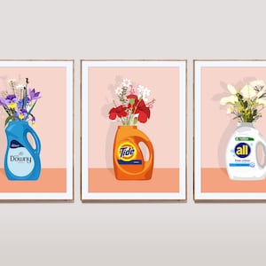 May include: Three framed prints of floral arrangements in detergent bottles. The bottles are labeled "Downy", "Tide", and "All Free Clear".