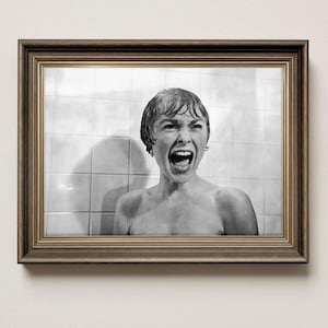 May include: A framed black and white photograph of a woman screaming in a shower. The image is in a brown wooden frame, and the background shows white tiles. The woman's mouth is wide open, and her expression is one of terror.