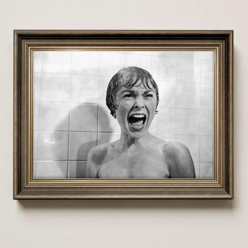 May include: A framed black and white photograph of a woman screaming in a shower. The image is in a brown wooden frame, and the background shows white tiles. The woman's mouth is wide open, and her expression is one of terror.