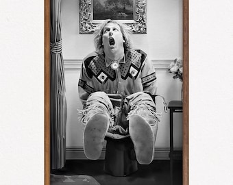 May include: Black and white framed print featuring a person with their mouth open, wearing a patterned shirt and fringed pants. The person is seated on a stool. A painting hangs on the wall behind them.