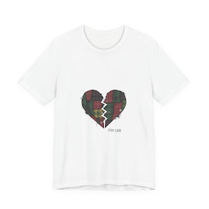 Puede incluir: Camiseta blanca con un diseño de corazón de retazos desgastado en tonos verdes, rojos y amarillos. El corazón está dividido por una línea irregular. Las palabras "STAY LOUD" están impresas debajo.