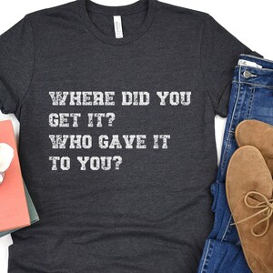 May include: A dark gray t-shirt with the text "WHERE DID YOU GET IT? WHO GAVE IT TO YOU?" printed in white.