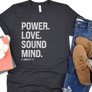 May include: A dark gray t-shirt with the text "POWER. LOVE. SOUND MIND. 2 TIMOTHY 1:7" printed in white.