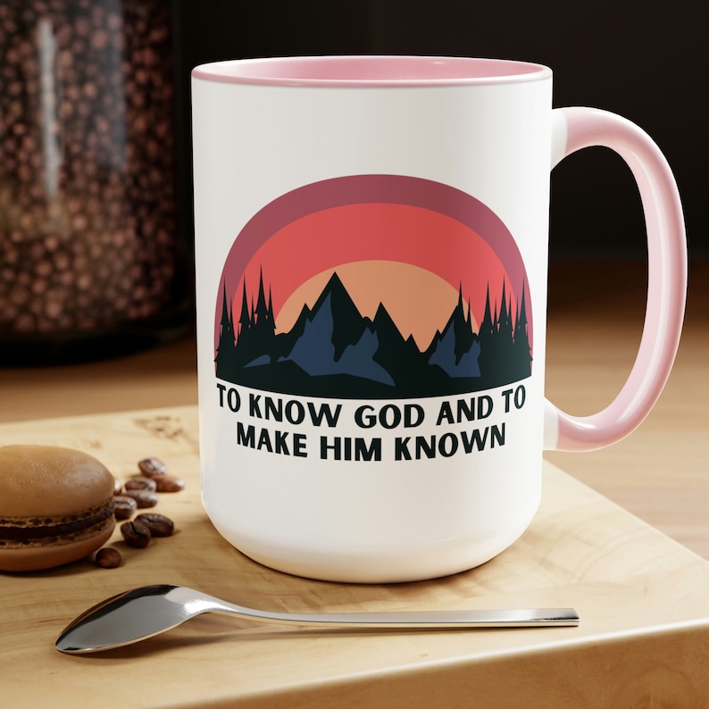 May include: White ceramic mug with a pink rim and handle. The mug features a retro-style mountain scene with a sunset and the text "To know God and to make Him known."