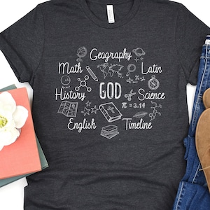 May include: A dark gray t-shirt with a white graphic design of school subjects and the word "GOD" in the center. The subjects include math, geography, history, English, Latin, science, and timeline.