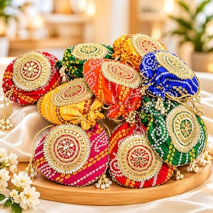 Può includere: Una collezione di borse rotonde colorate con coulisse, con intricati ricami dorati e dettagli di perline. Le borse sono in vari colori, tra cui rosso, giallo, verde e blu, e sono disposte su un vassoio di legno.