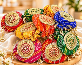 May include: A collection of colorful, round drawstring bags with intricate gold embroidery and bead accents. The bags are in various colors, including red, yellow, green, and blue, and are arranged on a wooden tray.