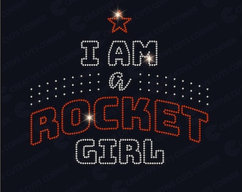 May include: Rhinestone design with the text "I AM a ROCKET GIRL" in orange and white. The design features a star at the top and a dotted background.