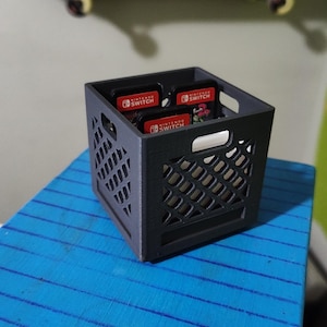 以下が含まれることがあります： グリッドパターンが付いた黒いプラスチック製の箱に、ニンテンドースイッチのゲームカートリッジが4つ入っています。カートリッジには、ニンテンドースイッチのロゴと「Nintendo Switch」の文字が印刷されています。