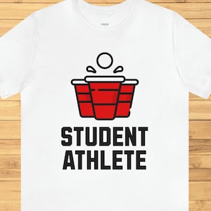 May include: White t-shirt with a red solo cup design and the text "STUDENT ATHLETE" printed in black.