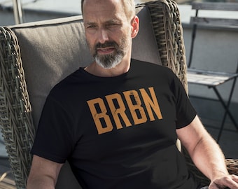 May include: A person wearing a black t-shirt with the word "BRBN" printed in orange on the front. The person is sitting in a wicker chair.