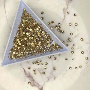 May include: A triangular tray filled with gold-coloured rhinestones, with a few scattered on a white marble surface.