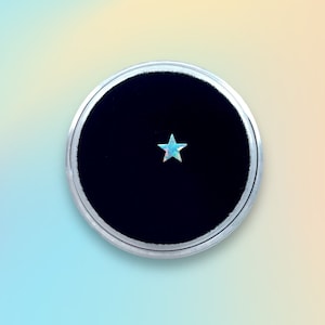 Op de afbeelding: Een kleine, iriserende blauwe stervormige opaal edelsteen getoond op een zwarte fluwelen achtergrond in een ronde zilveren display case.