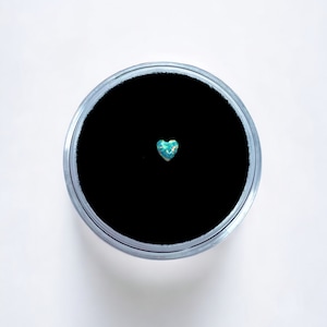 May include: A small, heart-shaped opal gemstone with a blue and green iridescent sheen, displayed on a black velvet background.
