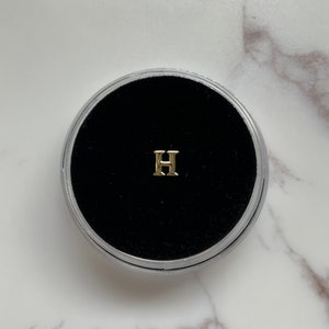 May include: A small gold letter H charm in a black velvet jewelry box.