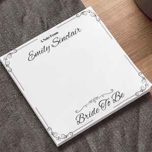 May include: A white notepad with a decorative border and the text "A Note From Emily Sinclair" and "Bride To Be" in black.