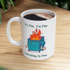 May include: White ceramic coffee mug with a blue and green cartoon image of a dumpster on fire. The text "It's Fine, I'm Fine" is above the image and "Everything Is Fine" is below the image.