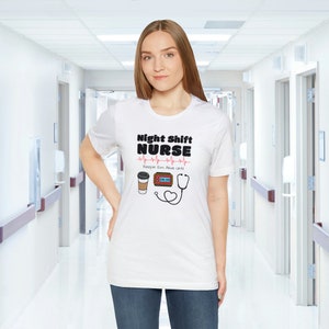 May include: White t-shirt with a black graphic that says "Night Shift Nurse" with a red heartbeat line and a coffee cup, clock, and stethoscope.