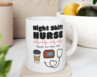 Può includere: Tazza in ceramica bianca con un design nero e rosso che dice "Night Shift Nurse" con un grafico di battito cardiaco, il testo "Keepin Em Alive Until" e uno stetoscopio, una tazza di caffè e un grafico dell'orologio.