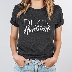 May include: A dark grey t-shirt with the text "DUCK Huntress" printed in white.