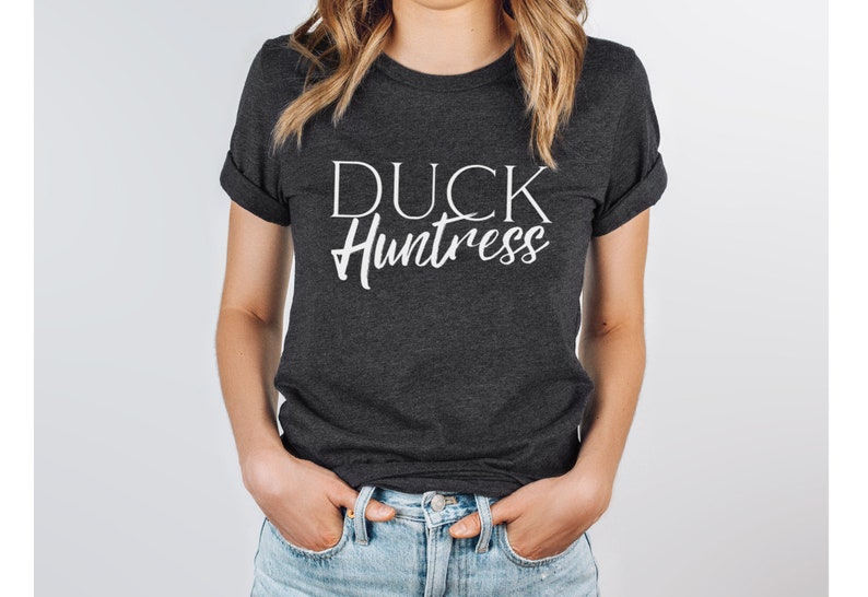 May include: A dark grey t-shirt with the text "DUCK Huntress" printed in white.