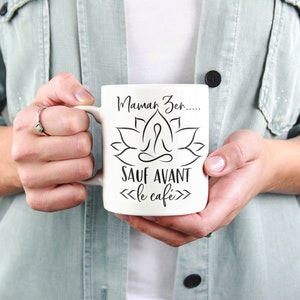May include: White ceramic mug with a black graphic of a lotus flower and a person meditating. The text on the mug reads "Mama Zen... sauf avant le cafe".