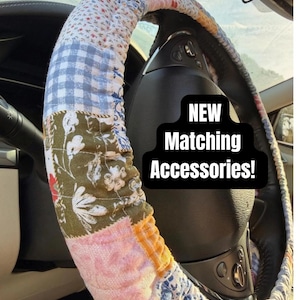 May include: A quilted steering wheel cover featuring a patchwork design of various floral, gingham, and solid fabric patterns in shades of pink, blue, olive green, and white. The text "NEW Matching Accessories!" is displayed in white on a black background.