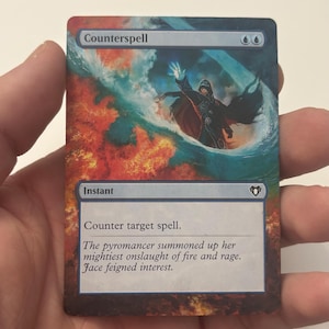 May include: A Magic: The Gathering card titled "Counterspell." The card features an illustration of a robed figure conjuring a spell amidst flames and water. The text reads "Counter target spell." and "The pyromancer summoned up her mightiest onslaught of fire and rage. Jace feigned interest."